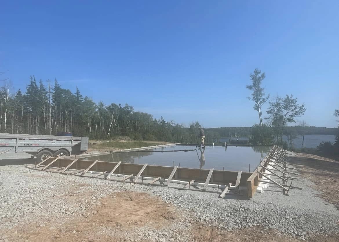 Worker finishing a fresh concrete pour beside the water