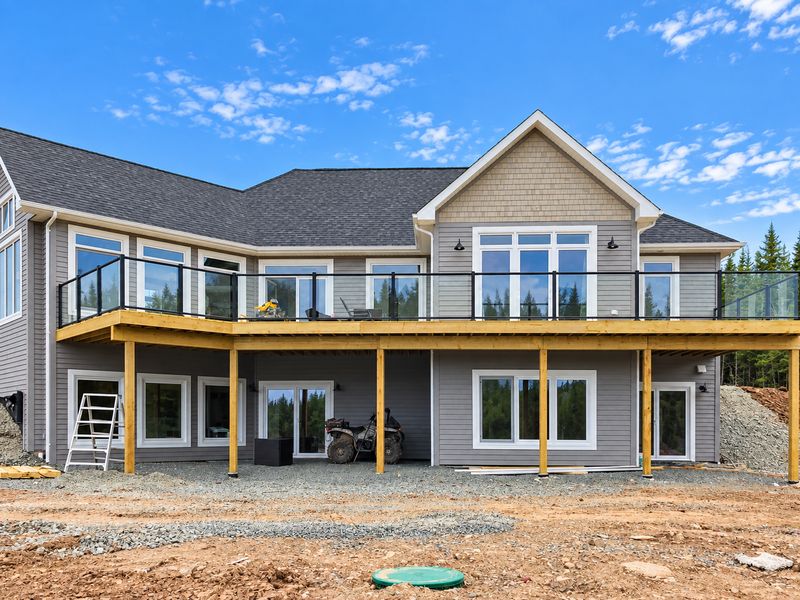 Back of a finished grey home with a large deck and glass railing, River Bourgeois