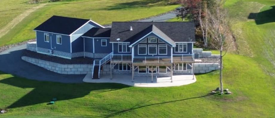 Aerial view of a finished blue home with a deck and stone retaining wall, St. George's Channel